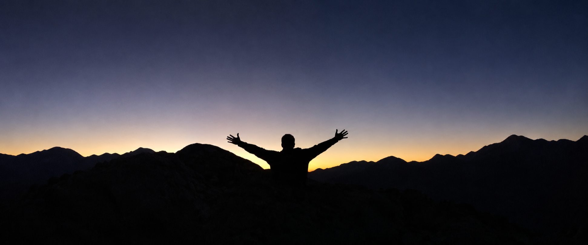 Dr. Alfred Ramirez, arms raised, silhouetted against a mountain sunset
